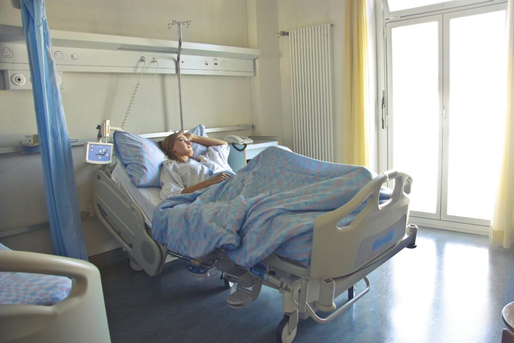 pexels-photo-3769151-3769151 A woman lying in a hospital bed in a bright, softly lit room, appearing to rest or recover.